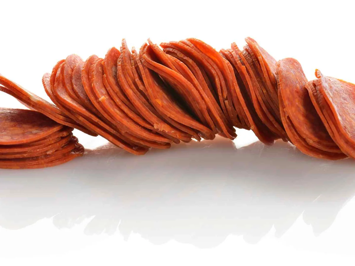 A fanned row of thin pepperoni slices on a white surface