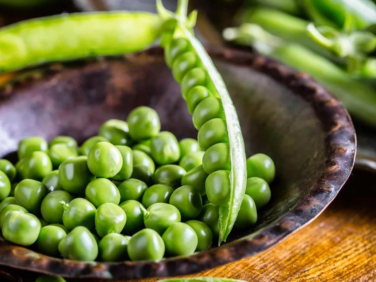 Green peas in a dark bowl with an open pea pod