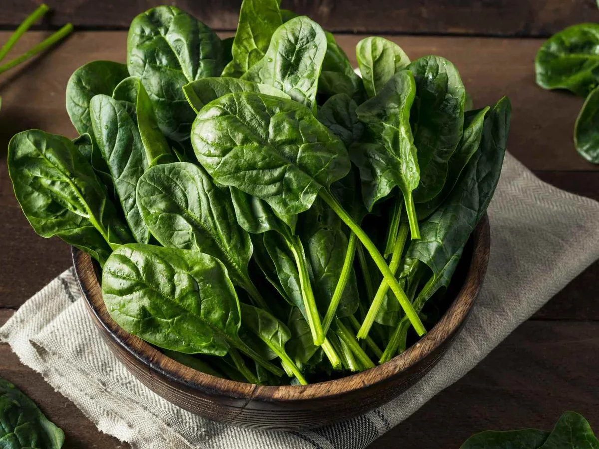 Fresh spinach leaves in a dark bowl on a wooden table