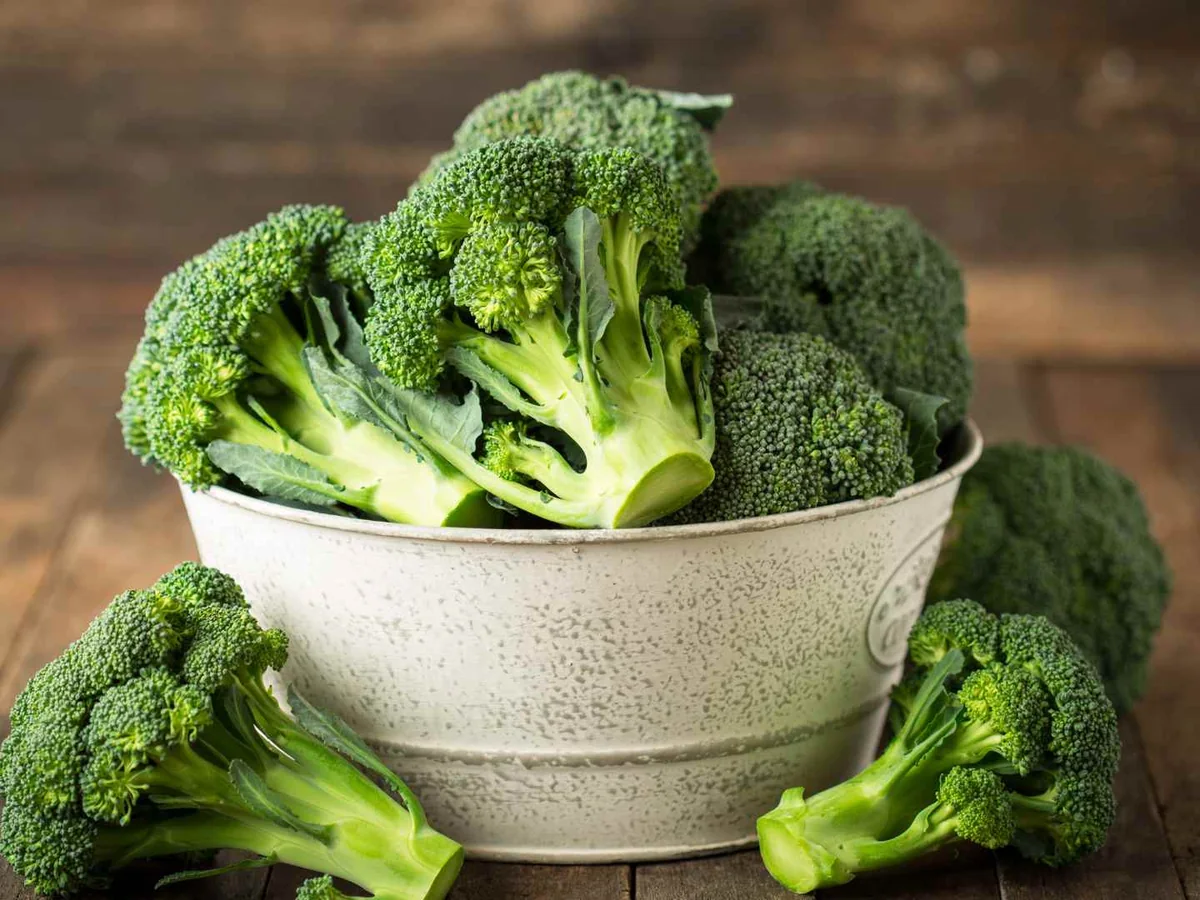 Fresh broccoli florets in and around a ceramic bowl