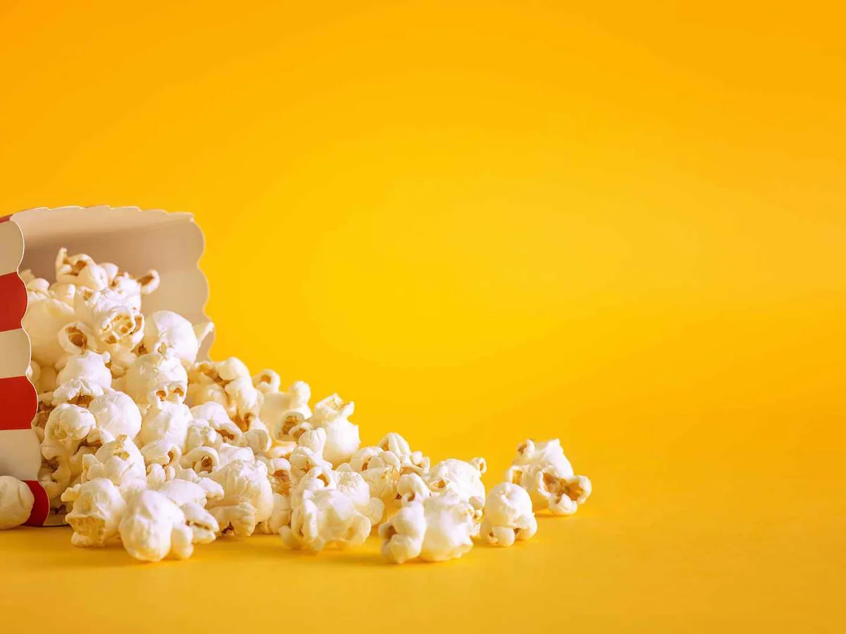 A tipped striped carton spilling popcorn on a yellow background