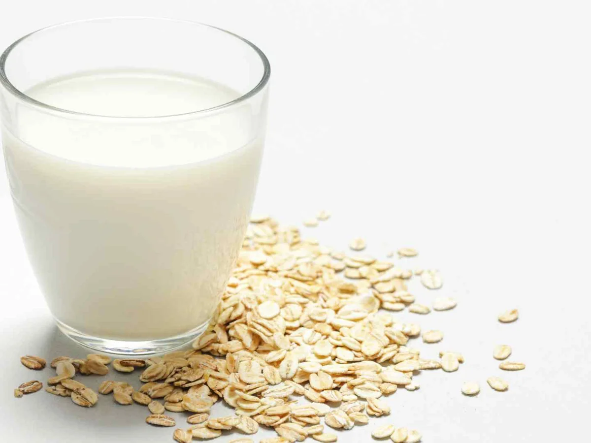 A glass of oat milk with loose oats on a white surface