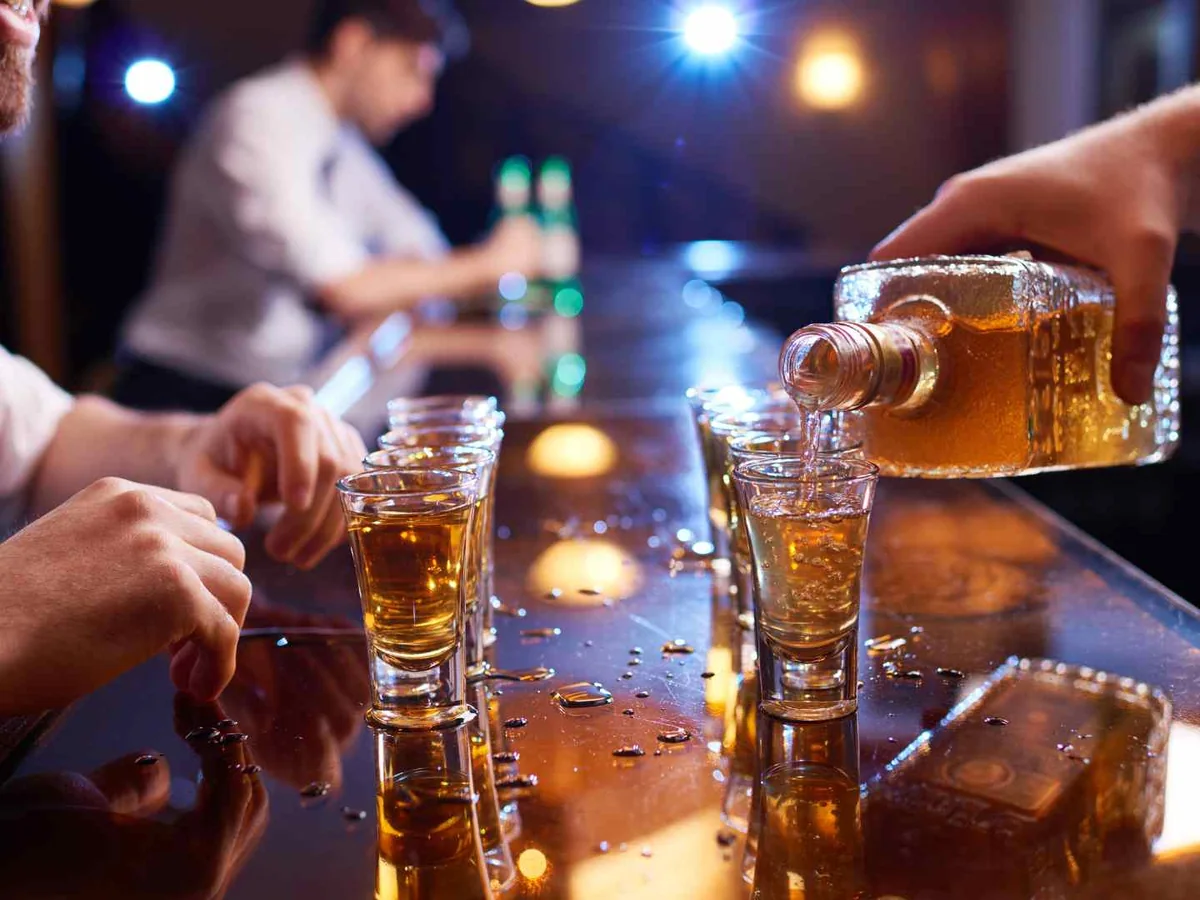 A bartender pouring amber liquor into small glasses