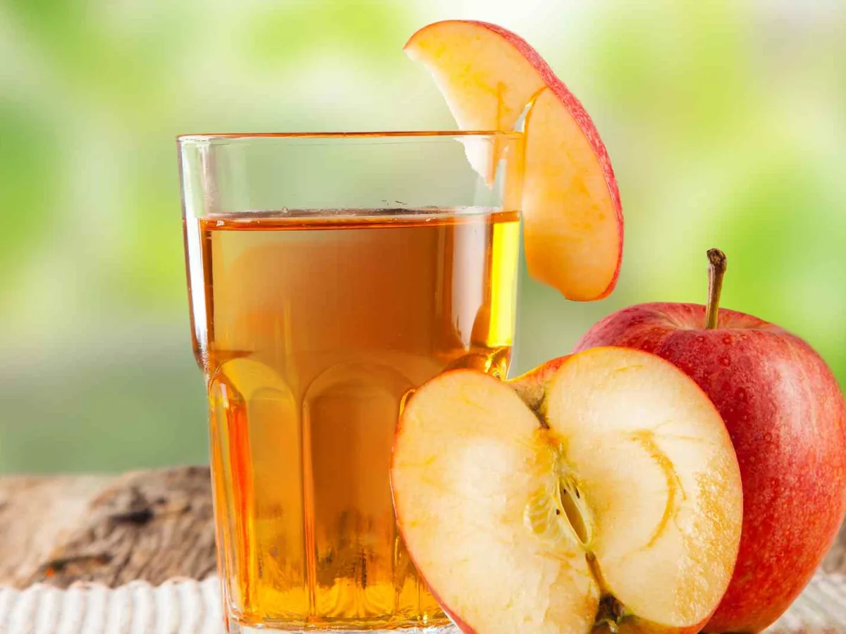 A glass of apple juice beside whole and sliced red apples