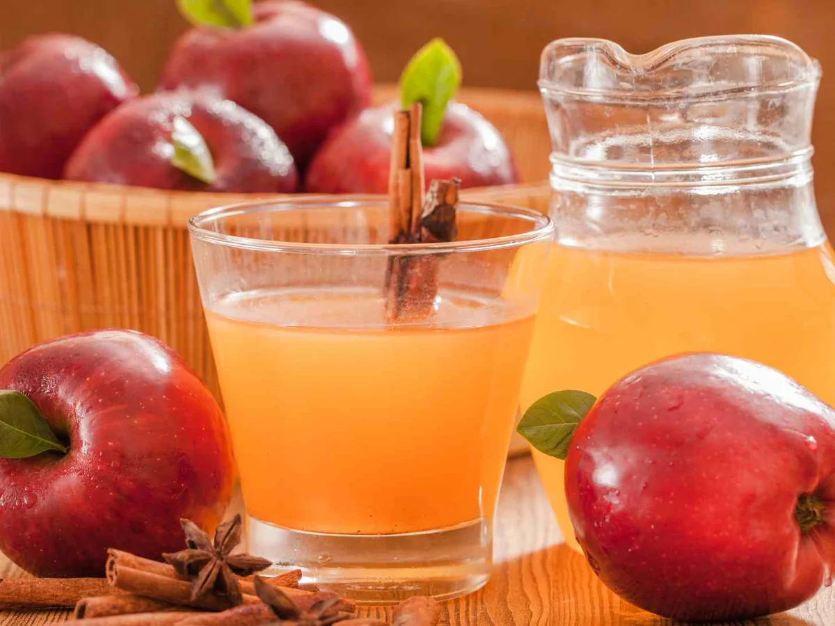 A pitcher and glass of apple juice surrounded by red apples