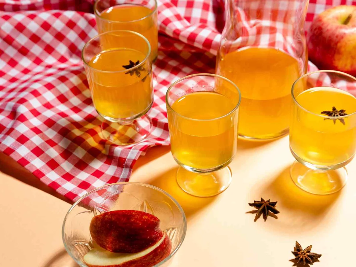 Small glasses of apple juice on a checked cloth with apples