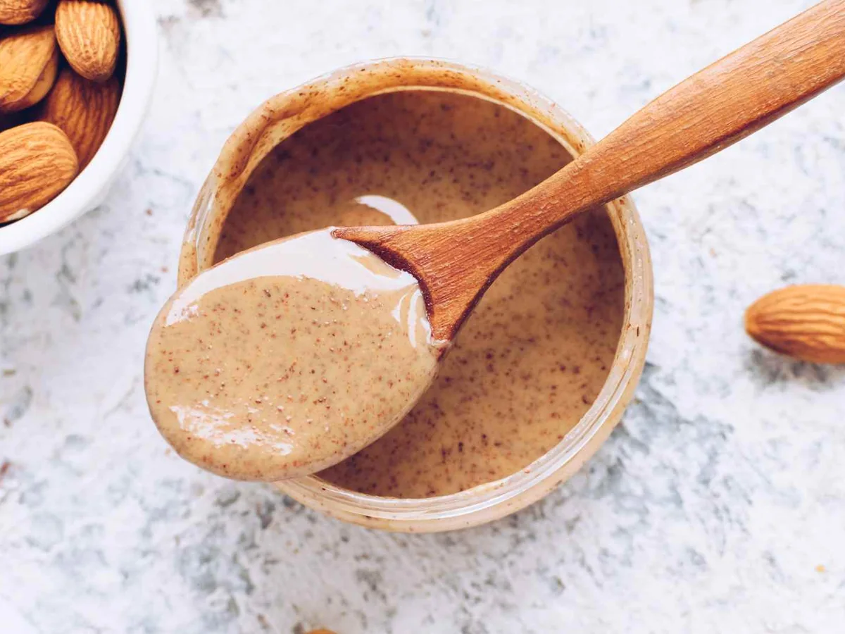 Almond butter in a wooden bowl with a spoon and whole almonds