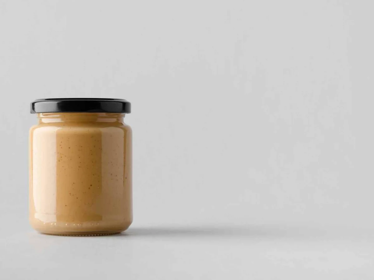 A plain glass jar of almond butter against a gray background