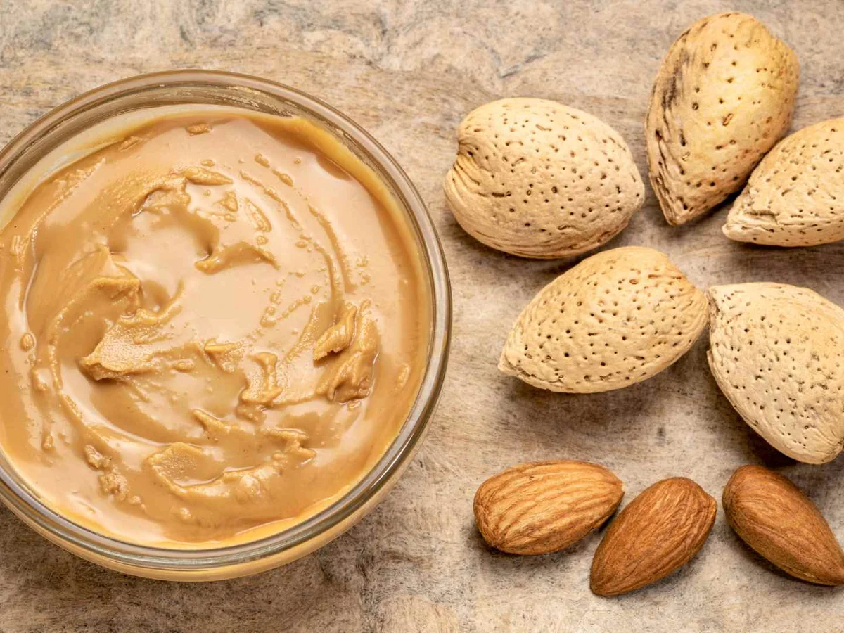 A glass bowl of almond butter surrounded by shelled almonds
