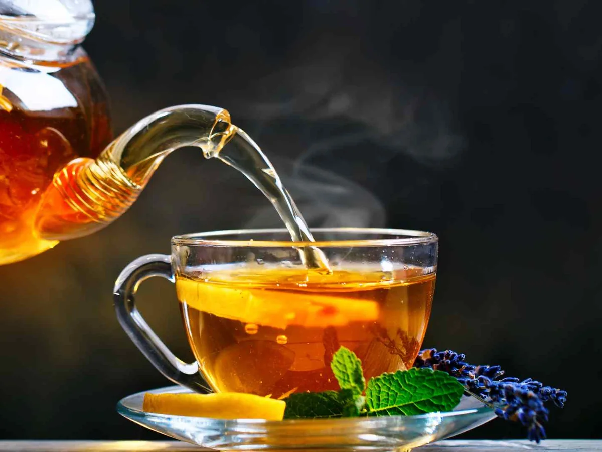 Amber tea pouring from a glass pot into a cup with lemon