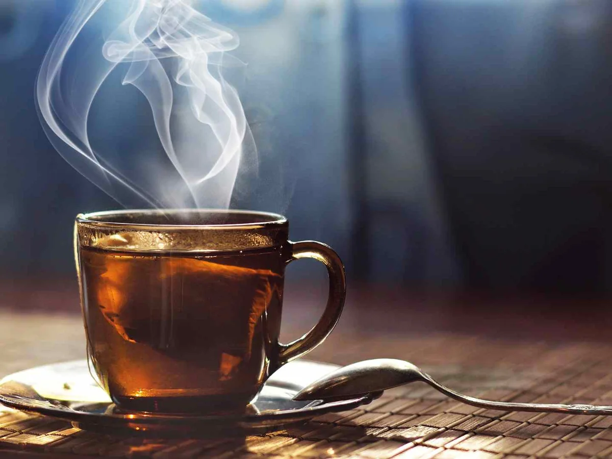 A steaming glass cup of tea on a wooden table