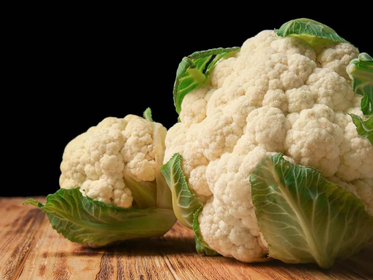 Whole cauliflower heads on a wooden table against black