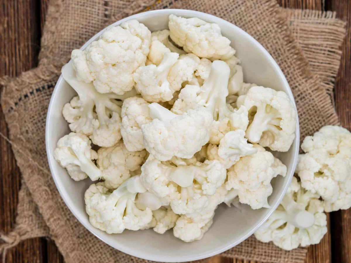 Cauliflower florets in and around a white bowl