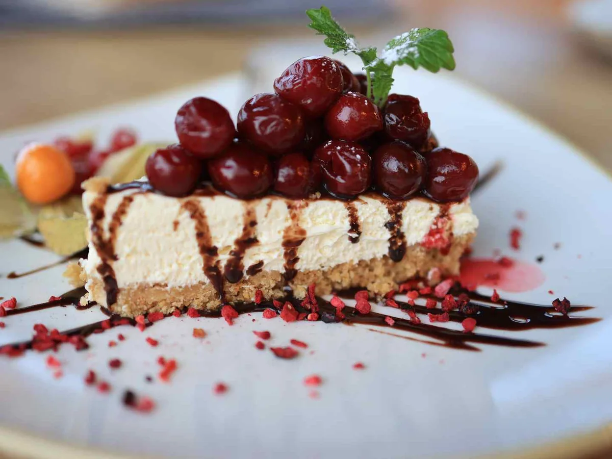 A berry-topped cheesecake slice drizzled with dark sauce