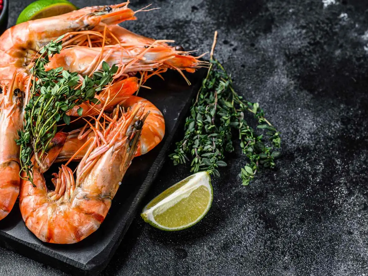 Whole cooked shrimp with herbs and a lime wedge on a dark tray