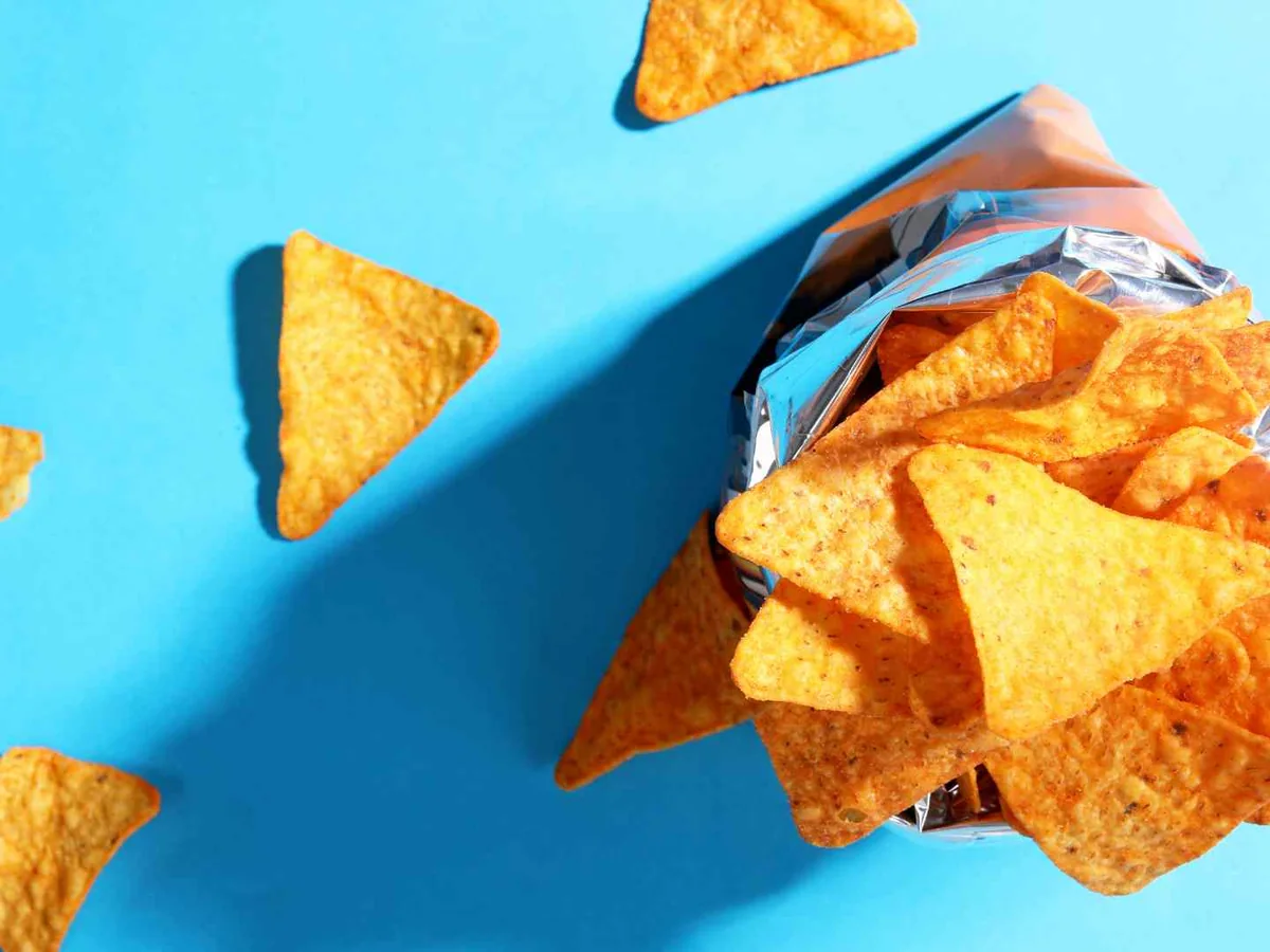 Orange triangular tortilla chips spilling from a plain bag