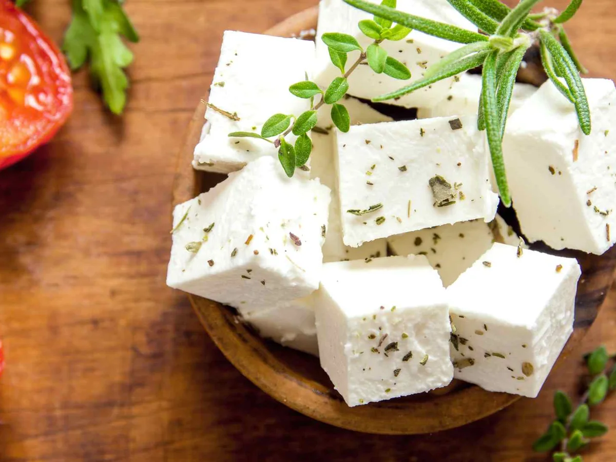 Herbed feta cubes beside tomatoes on a wooden board