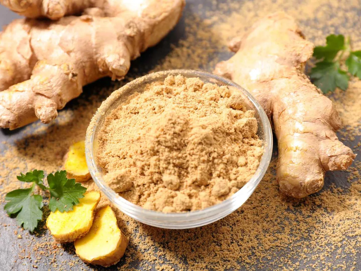 Ground ginger in a bowl surrounded by ginger roots