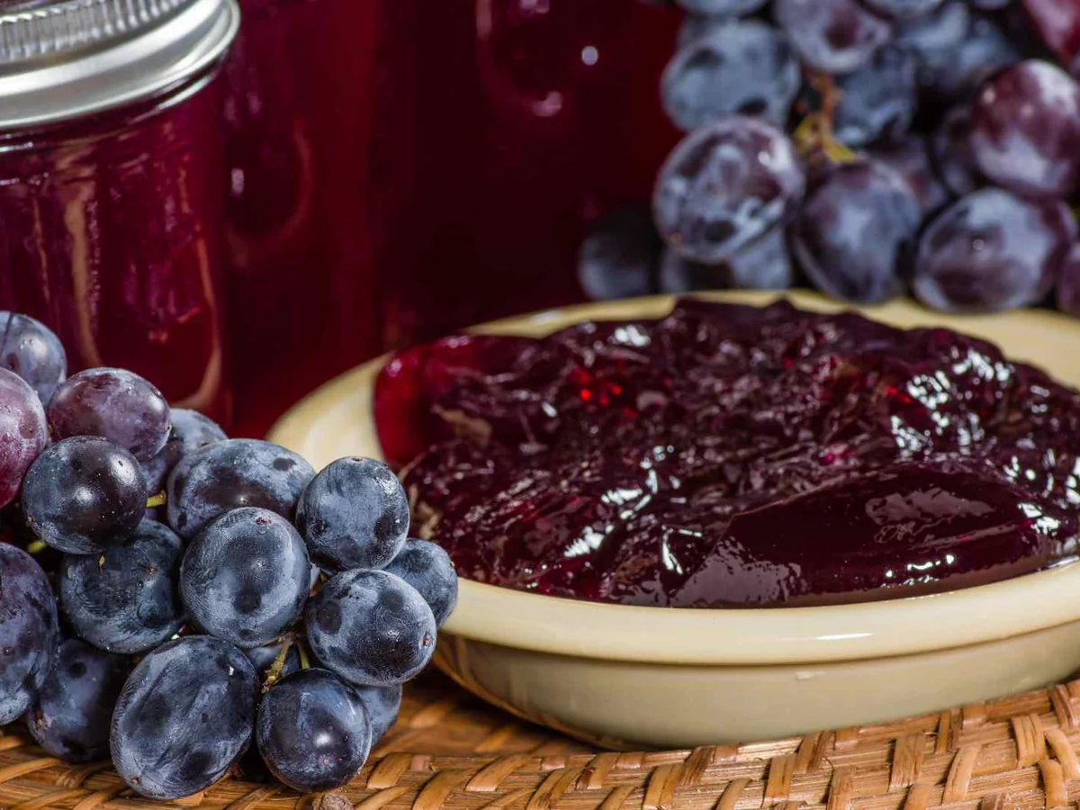 Grape jelly in a bowl beside purple grapes and jars