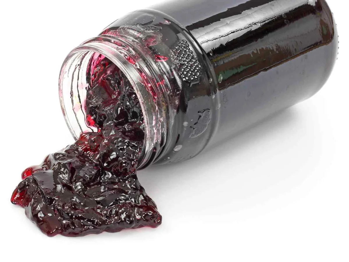 Dark grape jelly spilling from a tipped glass jar
