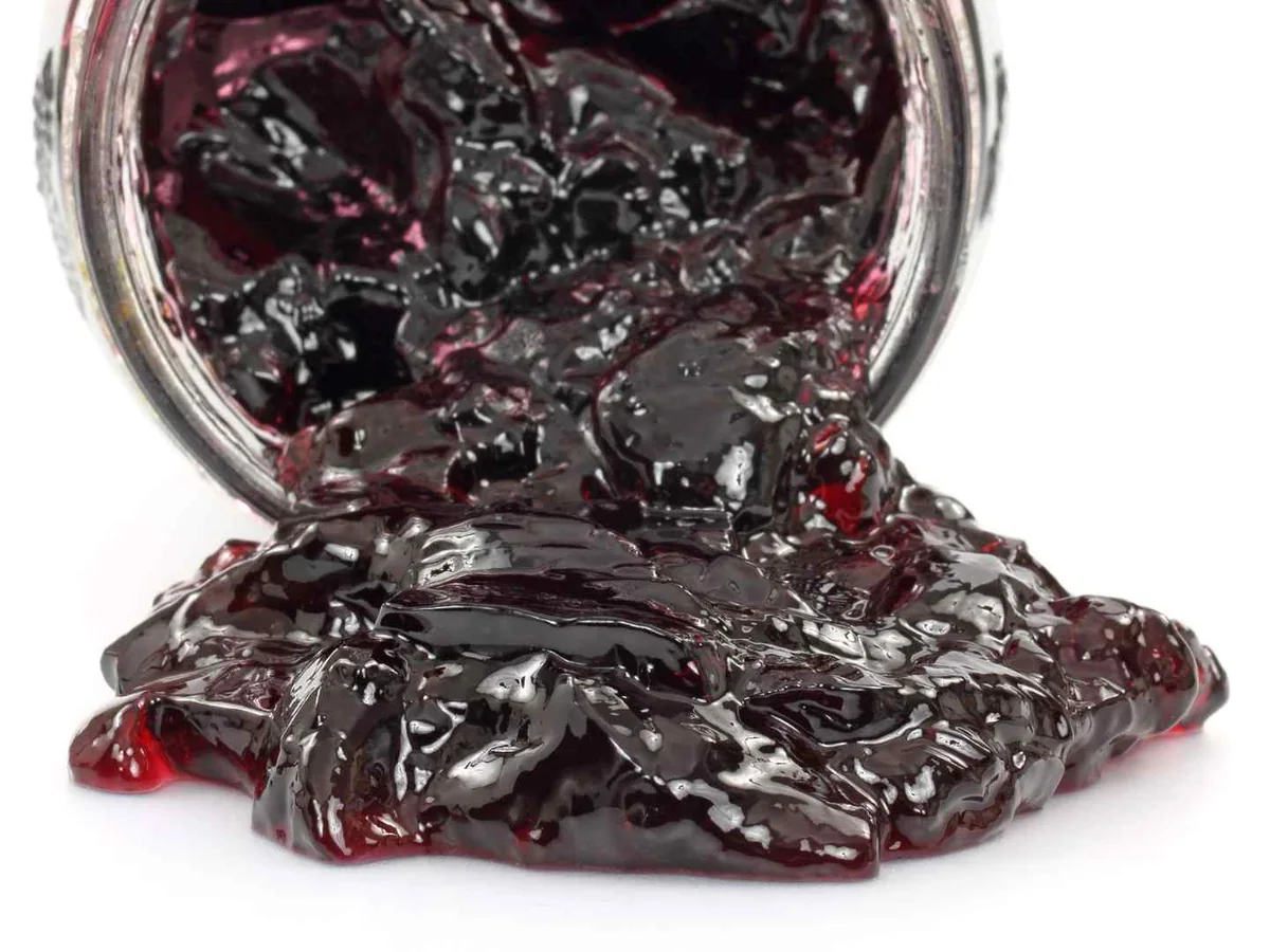 Dark grape jelly spilling from an upside-down glass jar