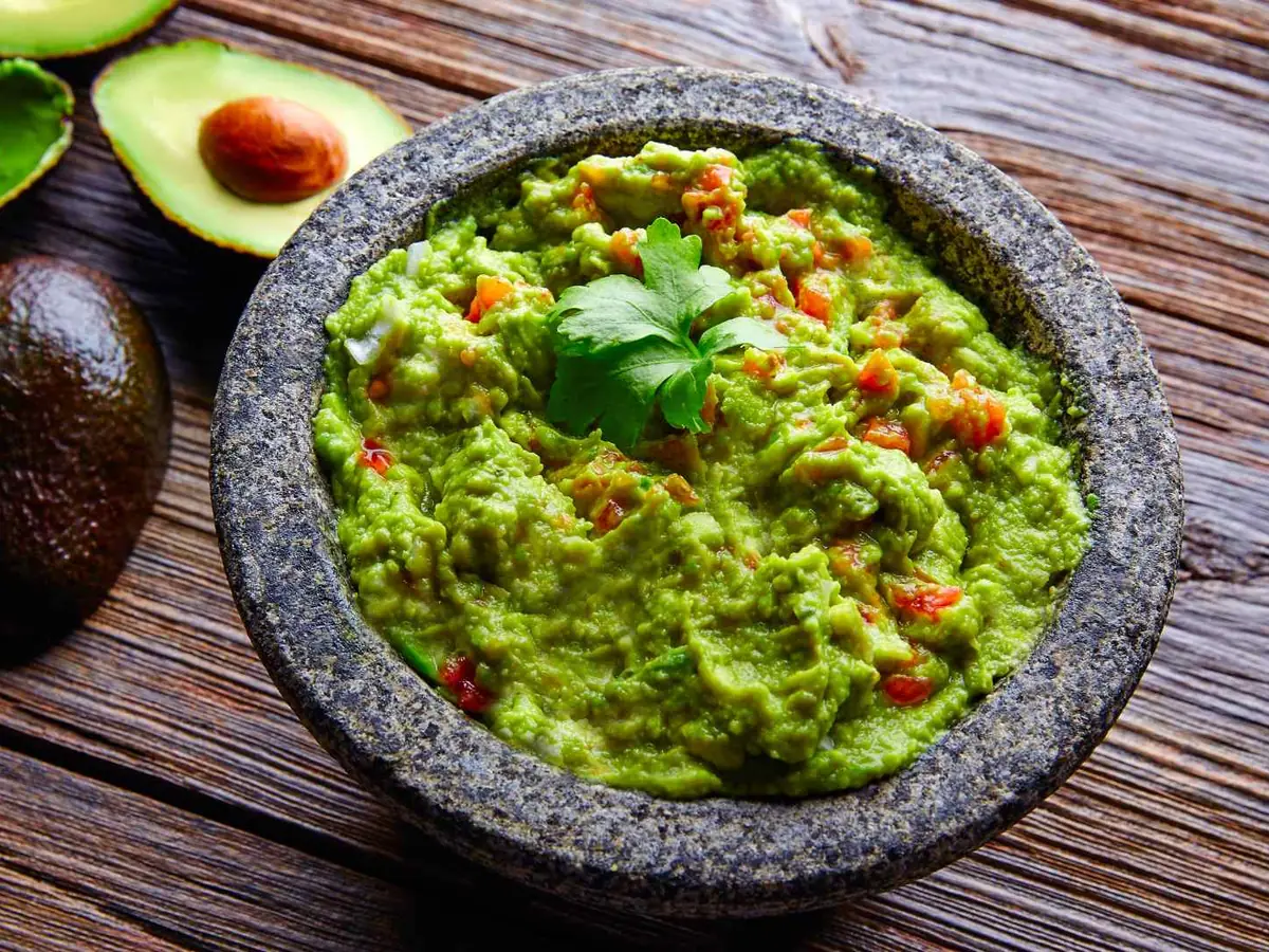 A stone bowl of chunky guacamole beside halved avocados