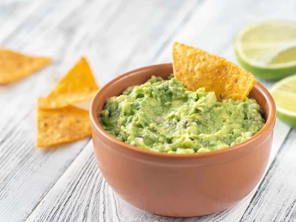 A bowl of guacamole beside tortilla chips and lime halves