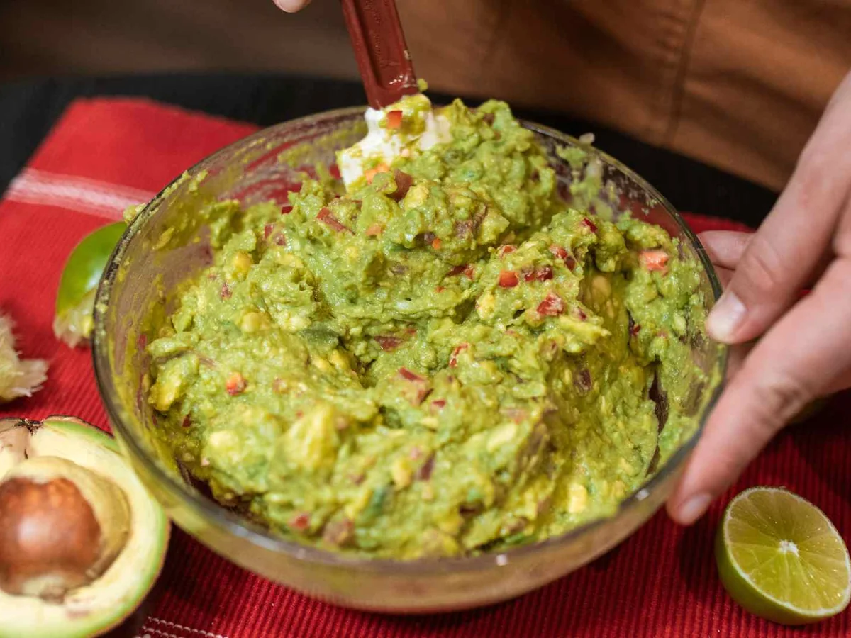 Hands stirring guacamole in a glass bowl