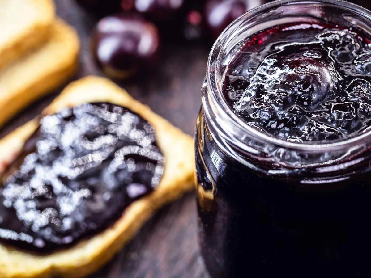 Dark berry jelly in a jar beside jelly-covered toast