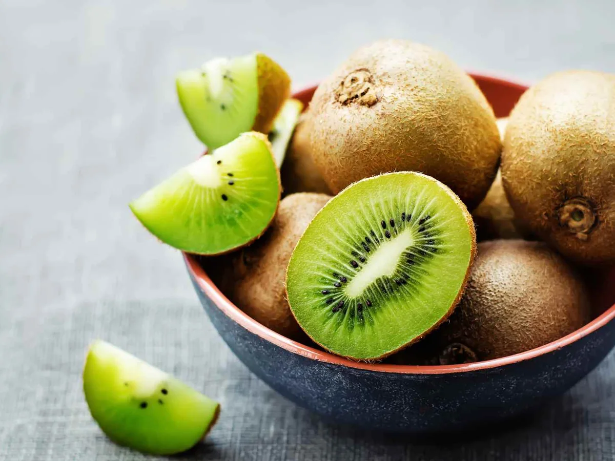 Whole and sliced kiwi fruit in a dark bowl