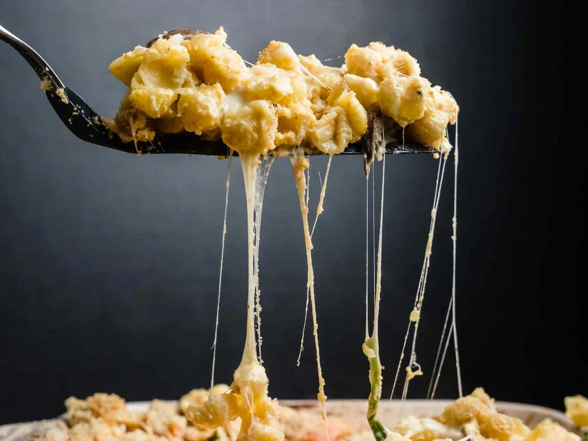 A fork lifting stringy macaroni and cheese against black