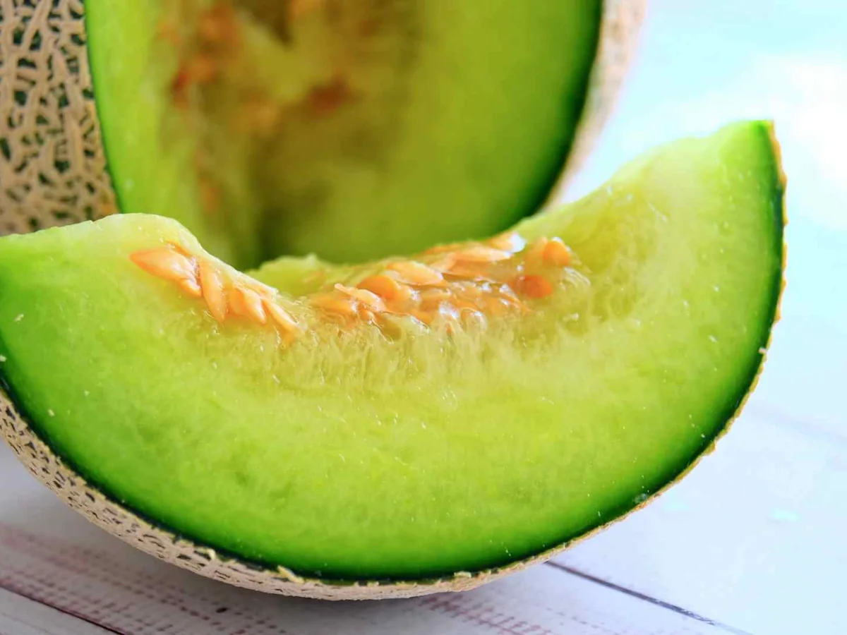 A sliced green-fleshed melon wedge beside its rind