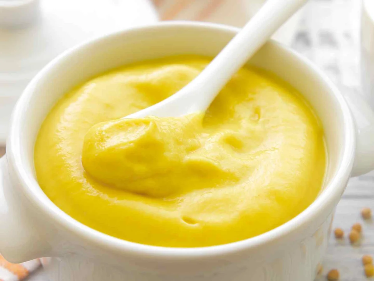 Creamy yellow mustard in a white bowl with a spoon