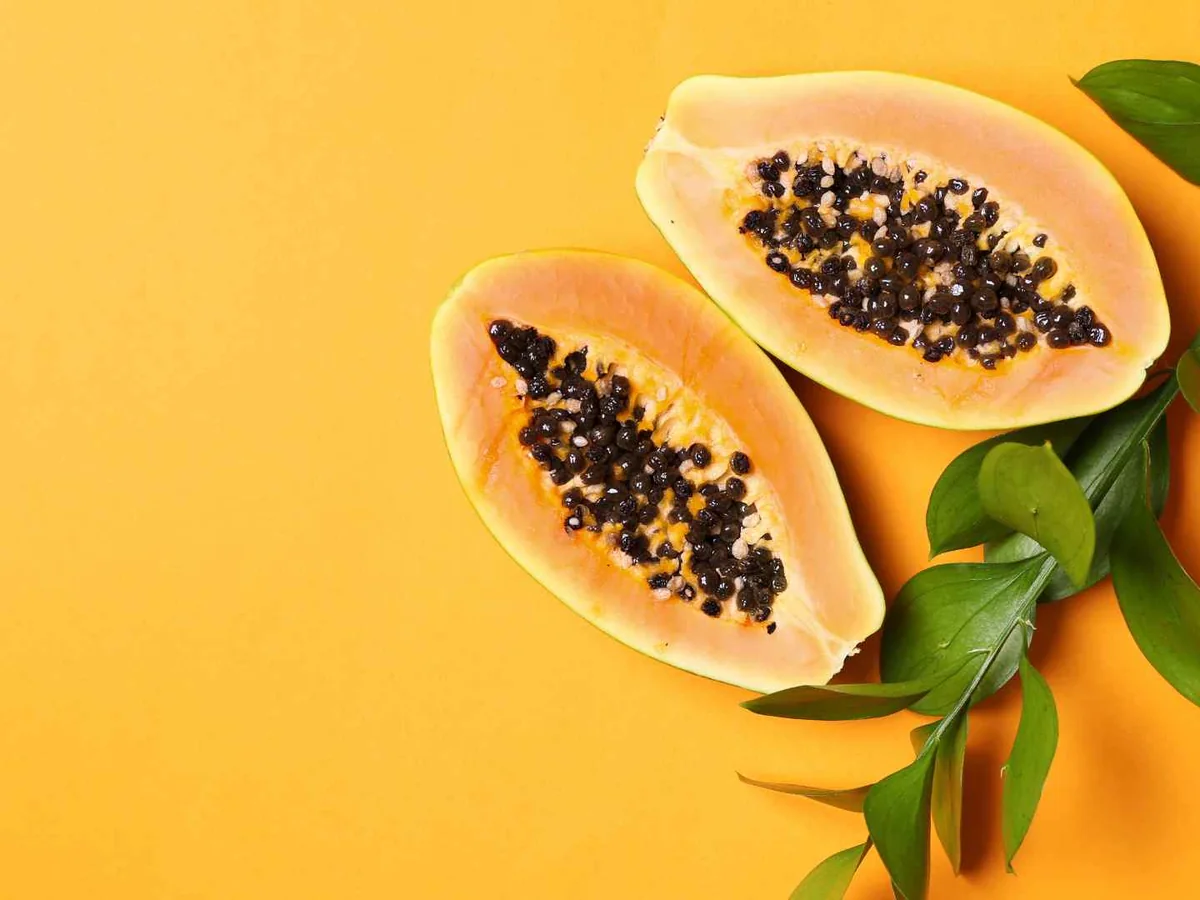 Halved papayas with black seeds on a yellow background
