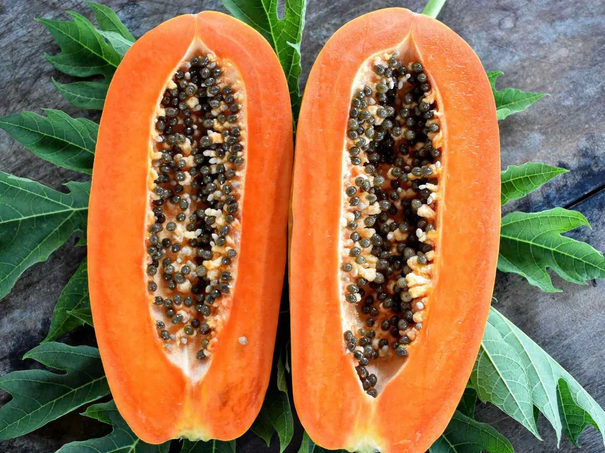 Two halved papayas with black seeds on green leaves