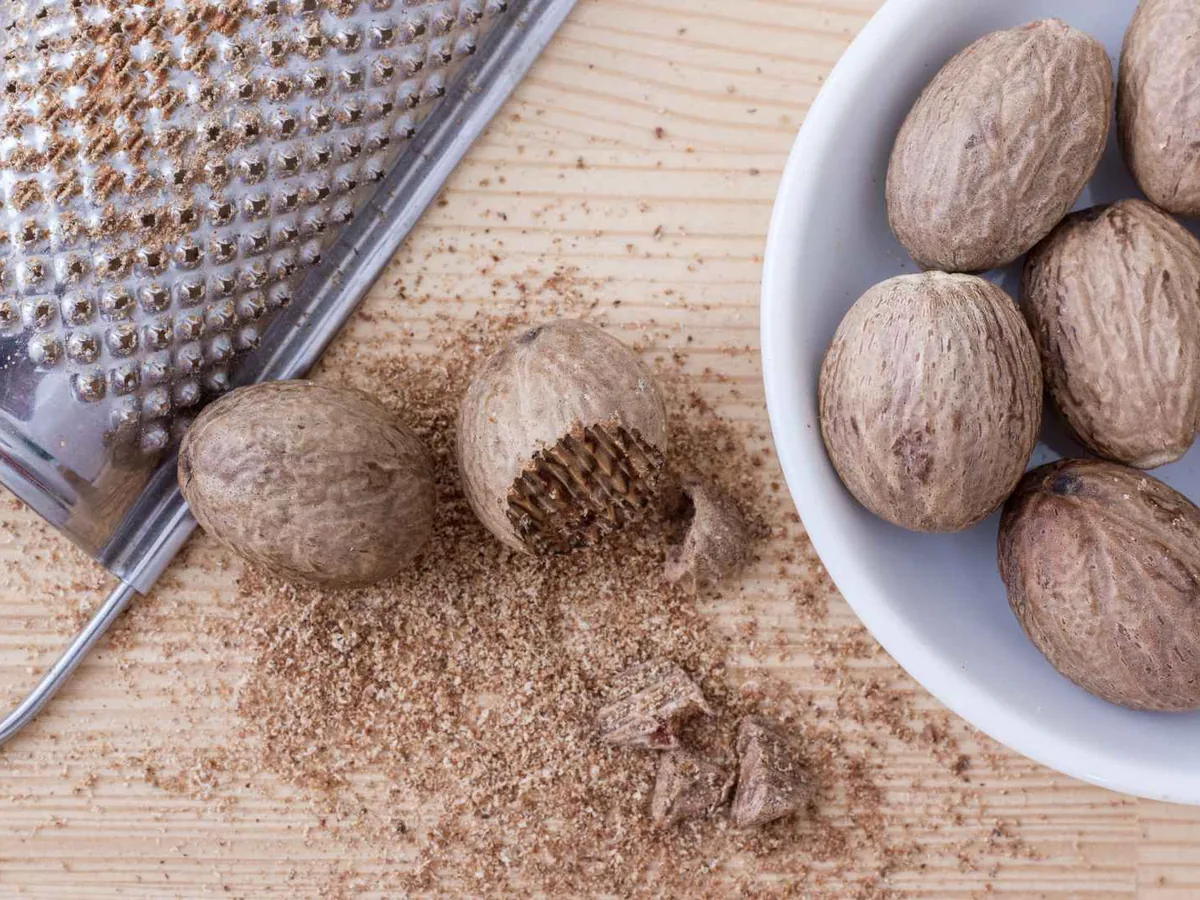 Whole nutmegs beside a grater and ground nutmeg