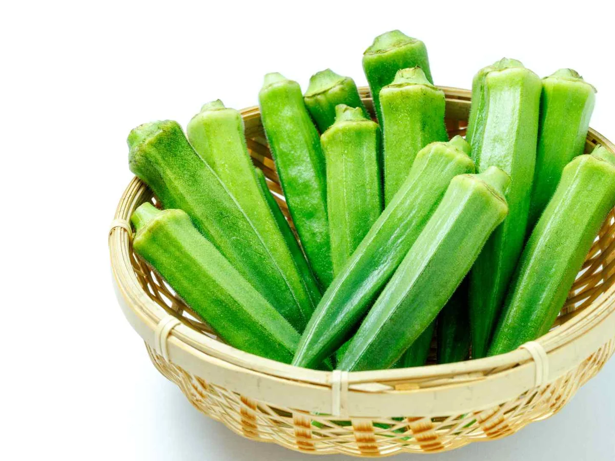 Whole green okra pods standing in a woven basket