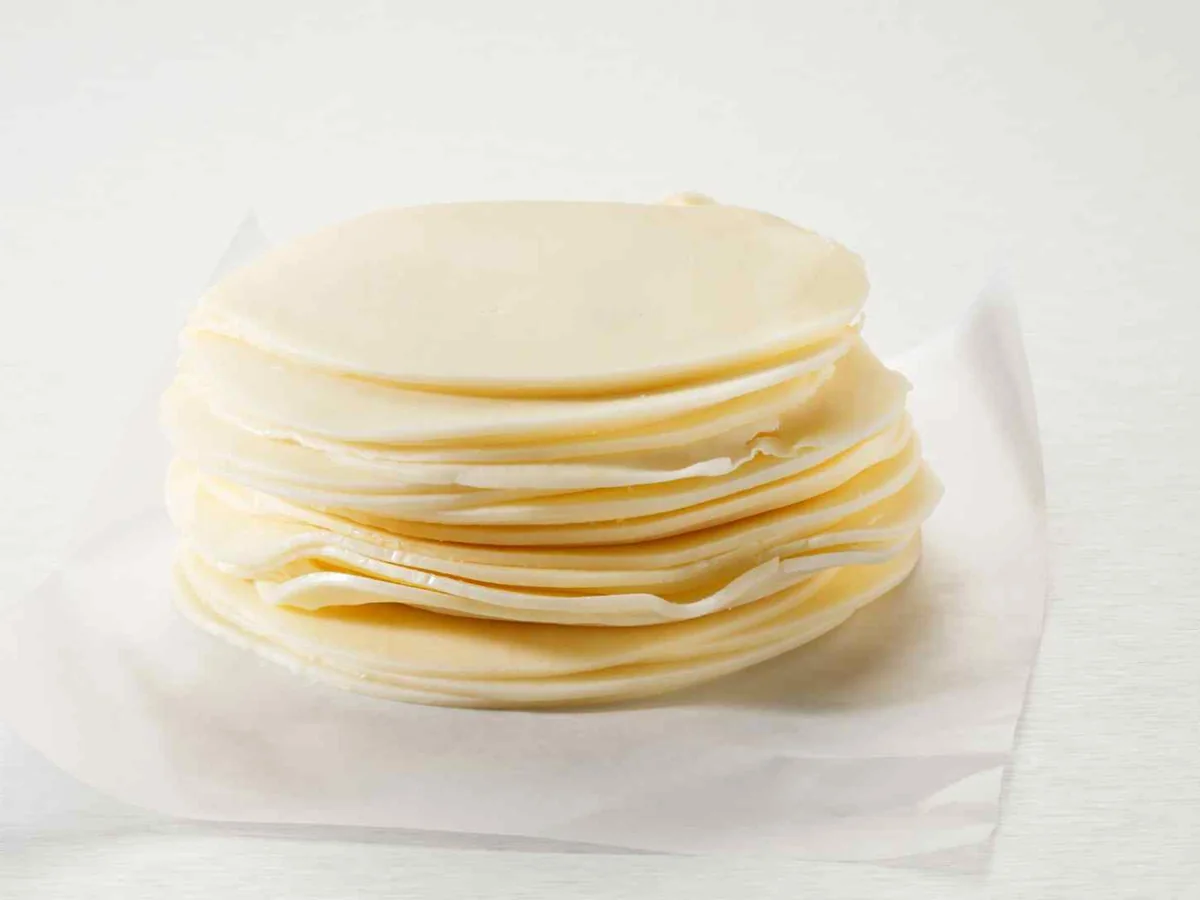 A stack of thin pale provolone slices on white