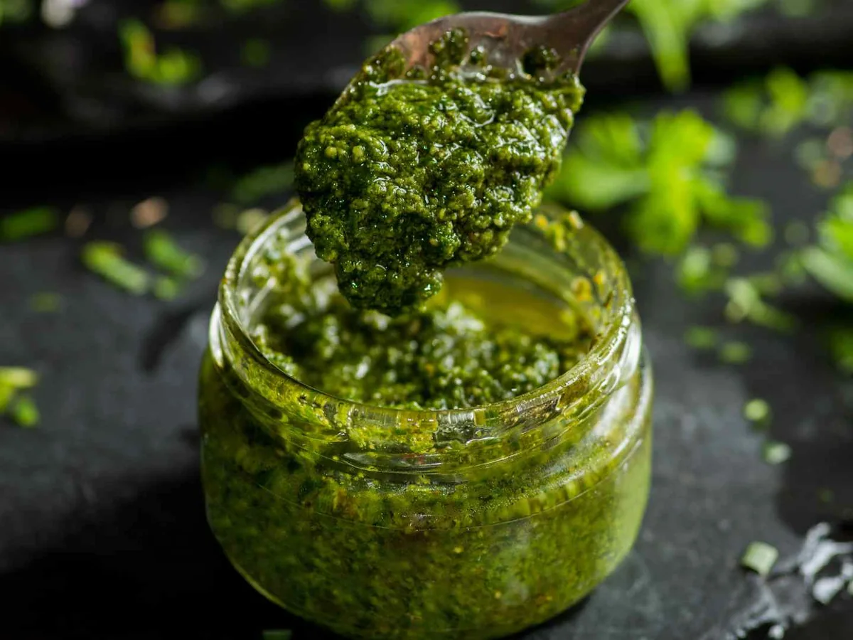 A glass jar of pesto on a dark surface