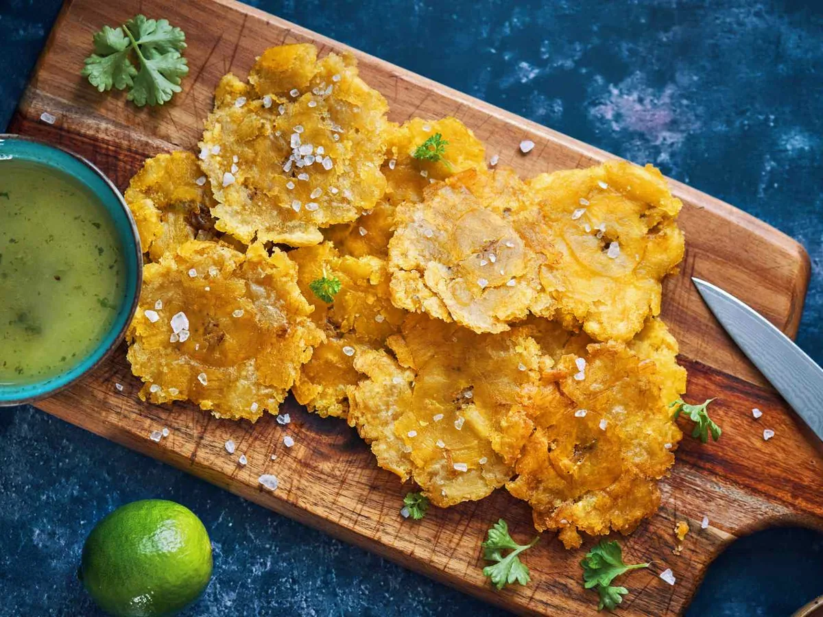 Fried plantain pieces on a board with green dipping sauce