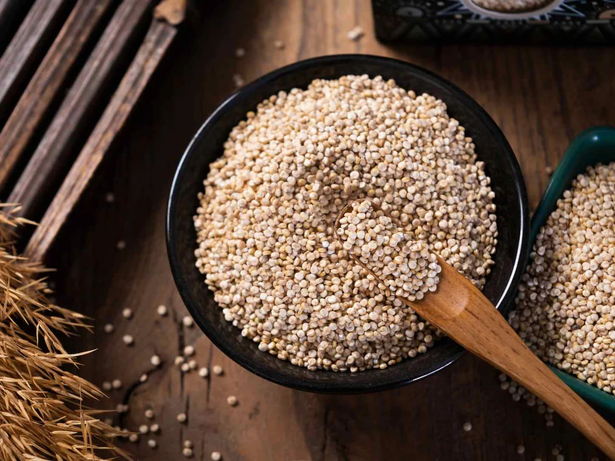 White quinoa grains in a black bowl with a wooden scoop