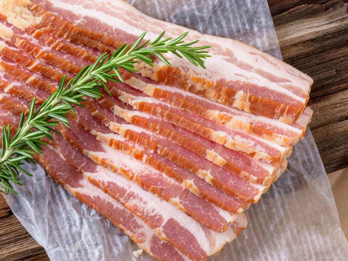 Raw bacon strips with rosemary on a wooden board
