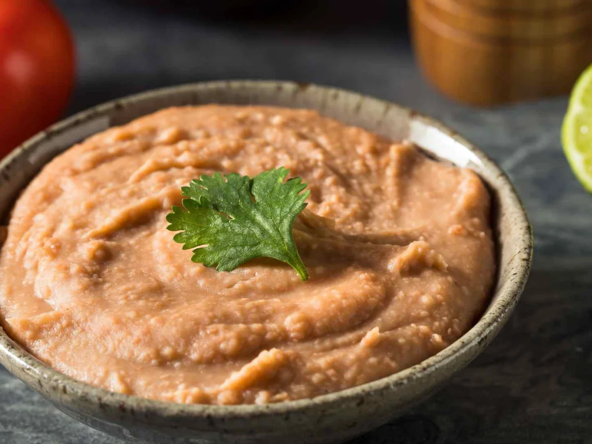 Refried beans in a dark bowl with lime and cilantro
