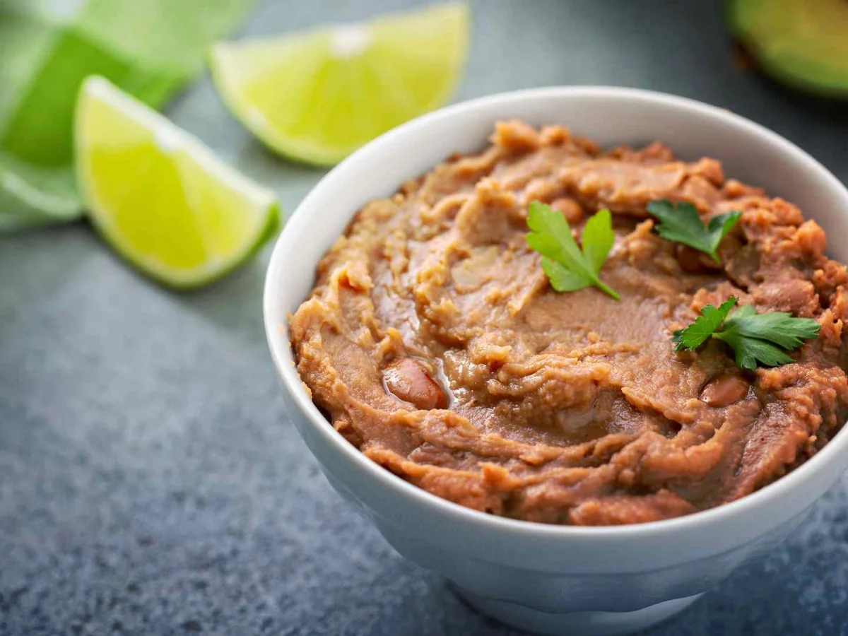 Refried beans in a white bowl with lime and cilantro