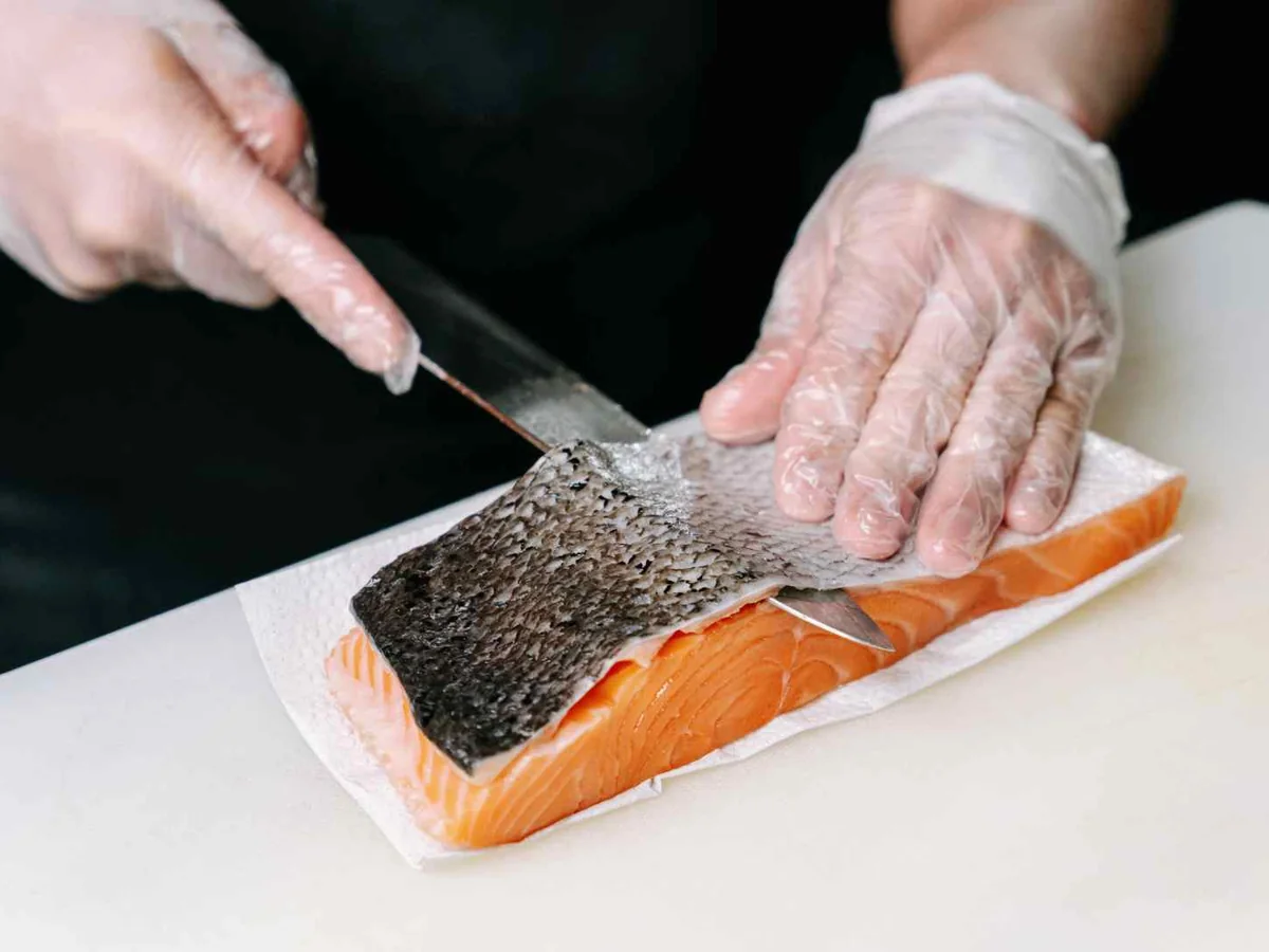 Gloved hands cutting the skin from a salmon fillet