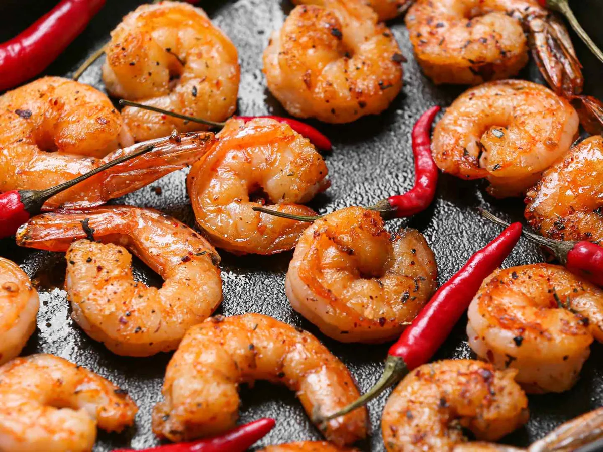 Cooked shrimp with tails in a skillet with red chiles