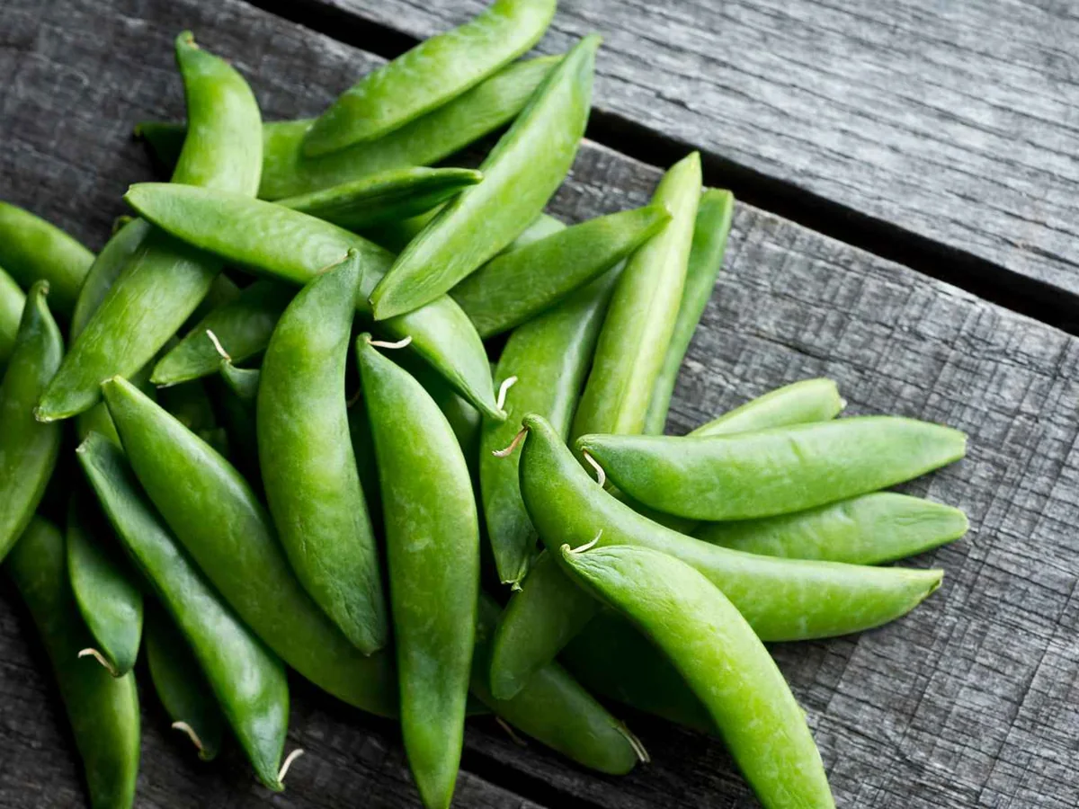 Fresh green snap pea pods on a dark wooden table