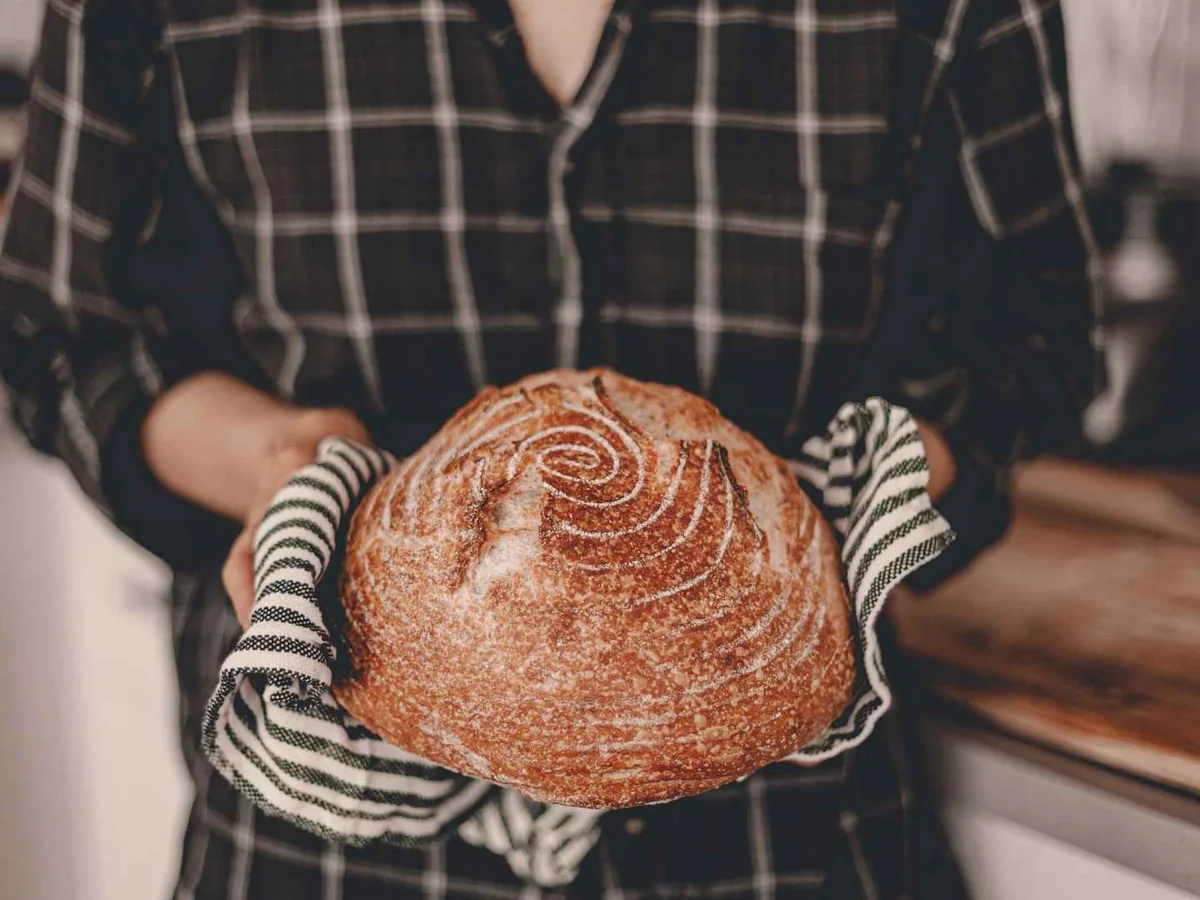 A person holding a round sourdough loaf in a striped cloth