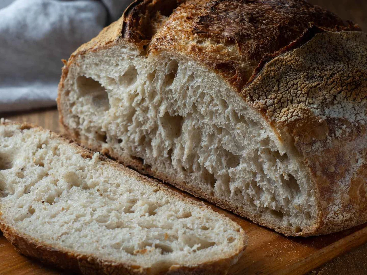 A sliced rustic sourdough loaf on a gray cloth