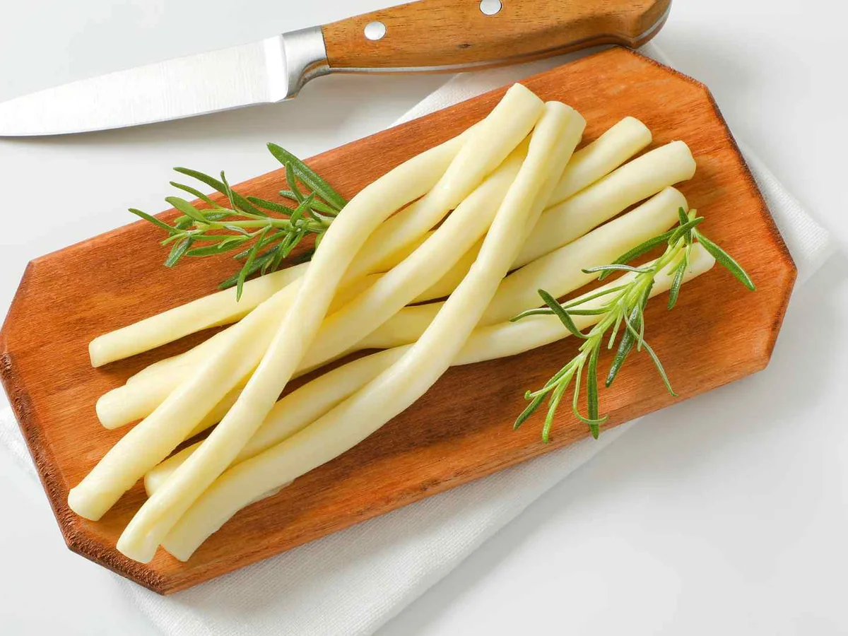 String cheese strips on a cutting board beside a knife